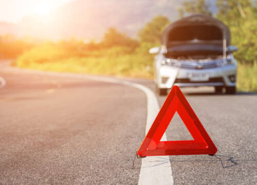 Red emergency stop sign and broken silver car on the road